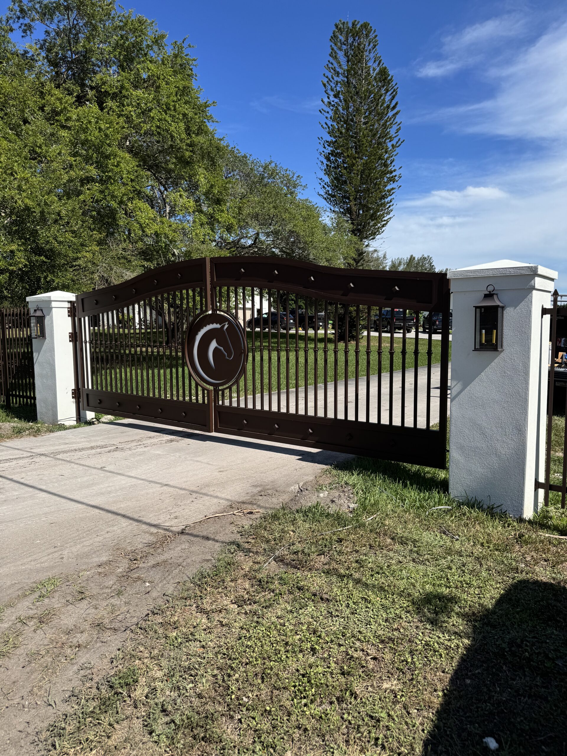 Ornate brown horsehead gate installed between white pillars.